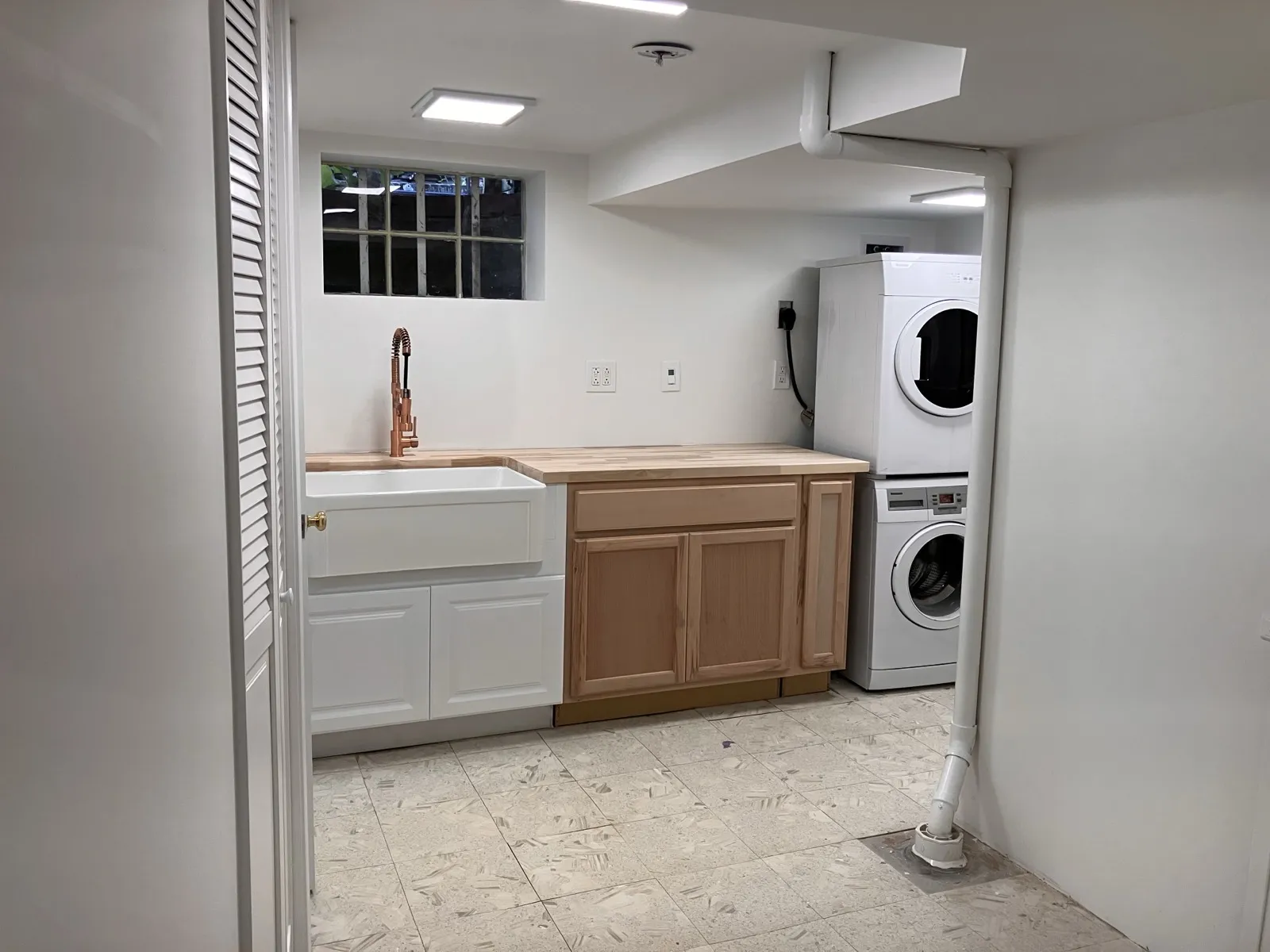 Laundry room with a white tile floor, a stacked washer and dryer and a farmhouse sink