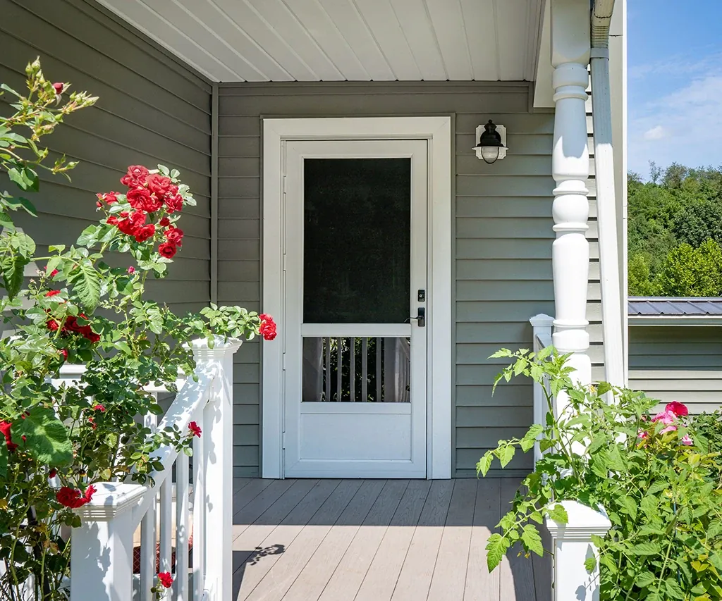 White storm door on a front porch with a white railing and red roses